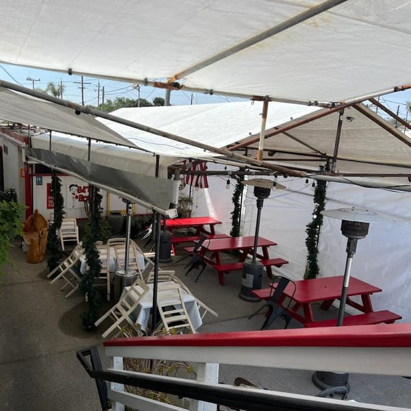 Outdoor dining area at Rock & Roll Diner with red picnic tables, white chairs, and patio heaters under a tent.