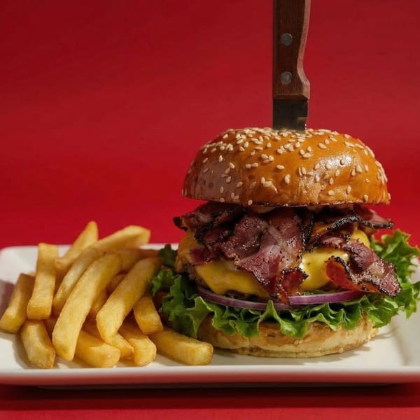 A Rock & Roll Diner burger with pastrami, cheese, lettuce, onion, and a knife, served with fries.