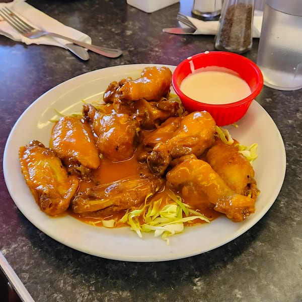 A plate of Rock & Roll Diner's buffalo wings with a side of ranch dressing on a dark table.